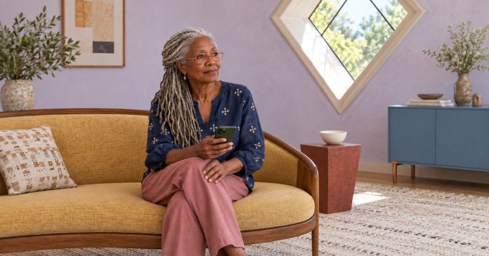 A mature woman considering a message while seated in a bright living room.